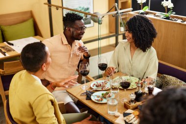 Arkadaşlar yemek masasındaki bir restoranda sohbet ederken eğlenirler..
