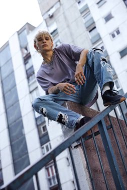 A teenage boy is sitting in an urban exterior surrounded by buildings.
