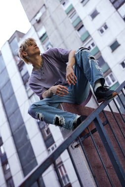 A teenage boy sitting on the wall surrounded by the buildings.