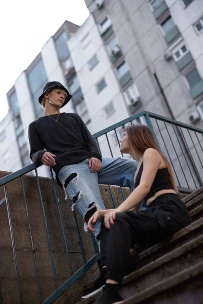 A teenage couple posing on the stairs in urban exterior.