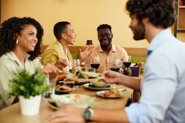 A group of multicultural friends eats dinner at the restaurant.