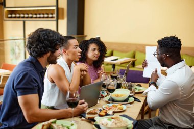 An African manager shows annual finances on paper while having a briefing with employees in a restaurant during lunch.