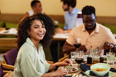 A happy Hispanic girl is eating dinner at the restaurant with her friend.