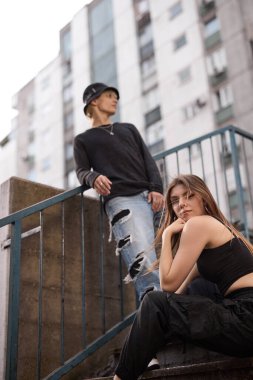 A teenage couple is posing outside on the stairs surrounded by buildings.