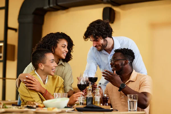 A small group of multicultural friends in a restaurant toasting with red wine.