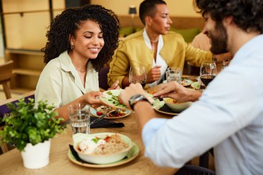 Cheerful friends are sharing food from the plate during a dinner party at the restaurant.