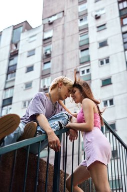 A lovely teenage couple is hugging and snuggling outside in an urban exterior surrounded by buildings and skyscrapers.