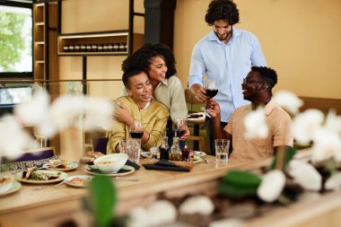 The best friends celebrate the happy event in a restaurant during dinner. They are laughing, bonding, and toasting with red wine.
