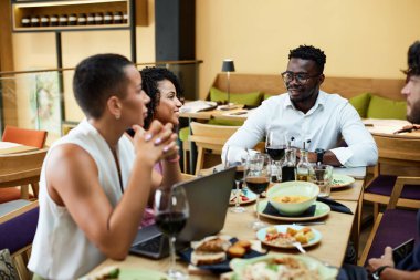 An interracial employer sits in a restaurant with his workers and has team building during business lunch.