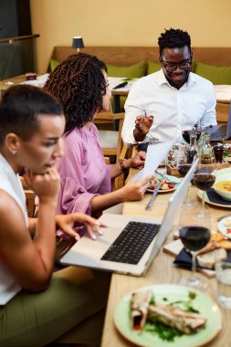 A cheerful group of multiracial colleagues having business lunch in a restaurant and working on the project.