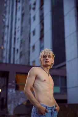 Portrait of a blonde shirtless teenage boy in the urban exterior.