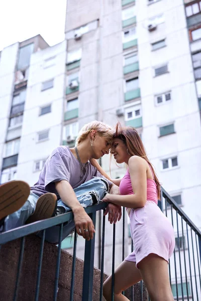 A lovely teenage couple is hugging and snuggling outside in an urban exterior surrounded by buildings and skyscrapers.