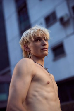 Portrait of a blonde shirtless teenage boy in the urban exterior.