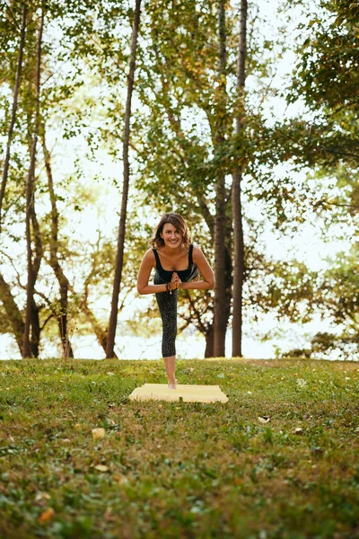 A happy woman is practicing yoga in the forest. She is balancing on one leg.