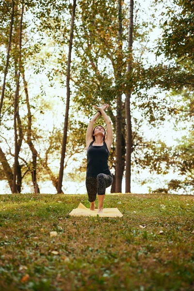 A flexible woman is practicing yoga in the forest. She is in the Crescent Lunge yoga pose.