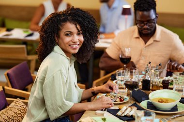 A Hispanic girl eats dinner in a restaurant with her friend.