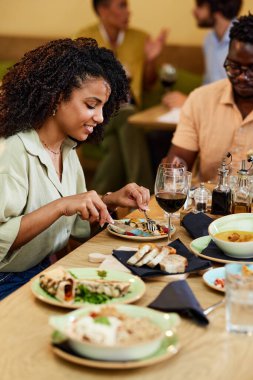 A Hispanic girl eats dinner in a restaurant with her friend.