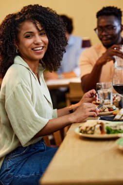 A Hispanic girl eats dinner in a restaurant with her friend.