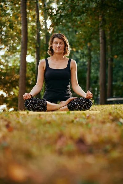 The calm woman is meditating in a lotus pose in the forest.