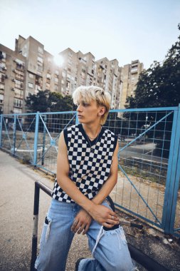 An urban teenager sits on the railing and chills at the street.
