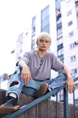 An urban teenager sits on the wall and chills at the street.