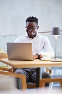 A freelancer is typing on the keyboard while smiling at the laptop in the cafeteria.