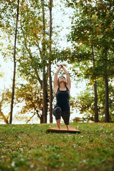 A slim woman practices yoga in the forest in warrior posture.