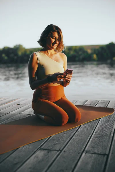 Fit Woman Kneeling Yoga Mat Texting Messages Phone Dock — Foto de Stock