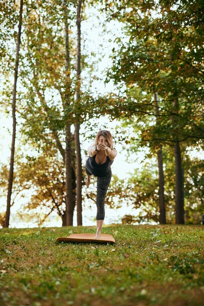 A happy woman is practicing yoga in the forest. She is balancing on one leg.