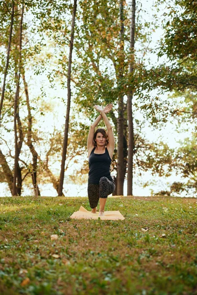 A flexible woman is practicing yoga in the forest. She is in the Crescent Lunge yoga pose.