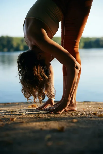 Silhouette of a flexible woman practices yoga on a dock.