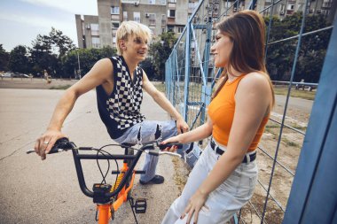A teenage boy is sitting on a bicycle while a girl is looking at him and flirting.