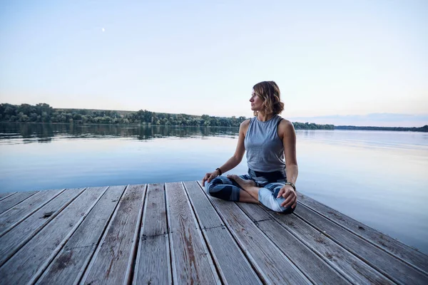 Yogi woman meditates and does breathing exercises while sitting on the dock.