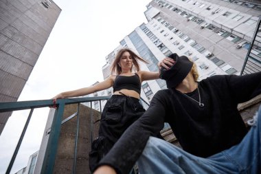 A teenage couple is posing outside on the stairs surrounded by buildings.