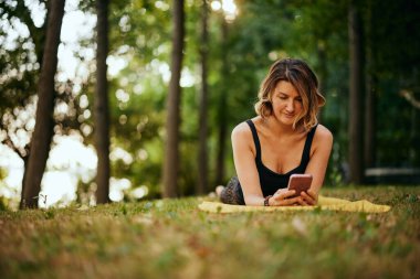 Formda bir yogi kadını ormanda yüzüstü yatıyor ve telefon kullanıyor..