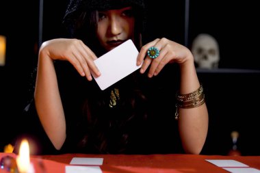 Siyah başlıklı kara cadı elinde sihirli kart, gizemli güzel kadın falcı geleceği kartla okuyor, korkutucu Cadılar Bayramı konsepti..