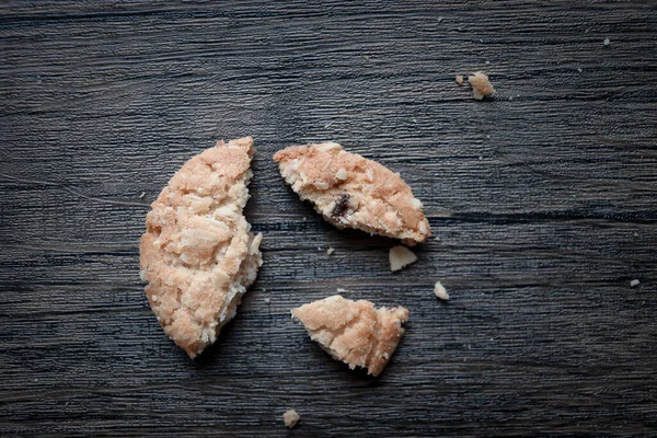 Broken oatmeal cookie with crumbs on wooden table.