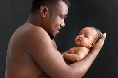 Babasının siyah arka planında kucağında küçük bir Asyalı Afrikalı yeni doğmuş bebek babasının kollarında sevimli bir bebeğin portresi, kucağında bir ebeveynin bebeği..