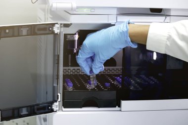 Yüksek Performans Sıvı Kromatografisi (HPLC) enstrümanı, kimya analitik deneyi içine tepsi koymak için eldiven tutan bir bilim adamı eli (küçük şişe) 