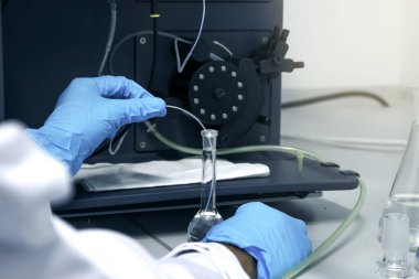 ICP çözeltilerindeki ağır metallerin seviyelerini belirlemek için deney yapmak için hacimli matara eldiveni kullanan mavi kimyasal koruyucu bir bilim adamı eli (İndüktif Eşleştirilmiş Plazma spektrometresi). Kimya laboratuvarında çalışan kimyager.