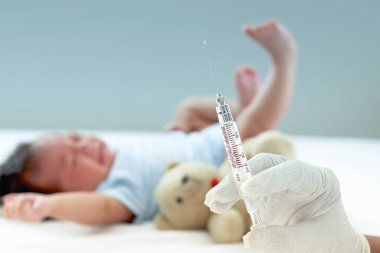 Doktor eli tıbbi eldiven takıyor ve elinde yeni doğmuş bebeğin bulanık arkaplanlı şırıngası var. Yatıp ağlıyor, bebek aşılıyor, çocuk aşısı konsepti veriyor..