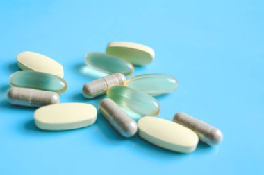 Kehribar rengi jel ilaç kapsülleri ve mavi arka planda sarı katkı besin hapları, ilaç tıbbi ve sağlık konsepti. 