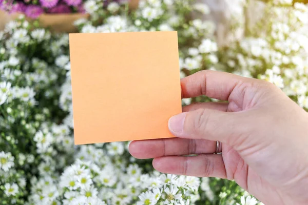 Blank note paper in hand on beautiful white cutter flower bouquet background, copy-space on card to put your message.