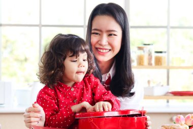 Mutlu gülümseyen genç anne ve küçük sevimli kızı sürpriz kırmızı hediye kutusunu açıyorlar, anne çocukla özel zaman geçirmekten hoşlanıyor. Sevgi ve sıcaklık aile kavramı.