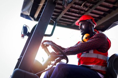 Fabrika fabrikasında parlak neon yelek ve kask giyen endüstriyel işçiler forklift kullanan Afro-Amerikan mühendis erkek lojistik kargo konteynerinde çalışıyor..