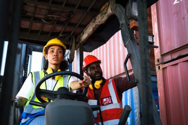 Sanayi işçileri fabrika fabrikasında forklift kullanan çelik yelek ve kask giyerler. İki Afrikalı Amerikalı mühendis ve kadın lojistik kargo konteynerinde birlikte çalışırlar..
