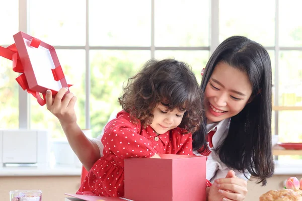 快乐的笑着美丽的年轻妈妈带着她可爱的小女儿打开惊喜的红色礼品盒礼物 妈妈喜欢和孩子一起度过特殊的时光 爱与温暖的家庭概念 — 图库照片
