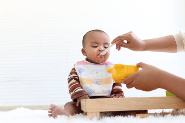 Anne, küçük tatlı Afrikalı Amerikalı bebeğini kaşıkla besliyor, küçük çocuk evde anne için sağlıklı ev yapımı bebek maması yiyor..