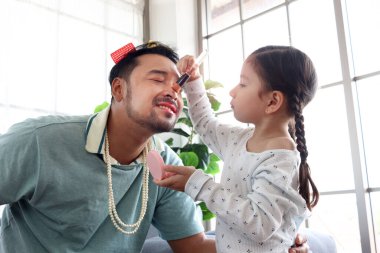Neşeli baba küçük sevimli kızıyla birlikte oynuyor, kız babasına makyaj yapıyor, oturma odasında kanepede oturuyor, aile tatilinde eğleniyor ve ayakta vakit geçiriyor..