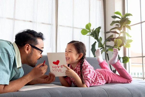 父亲节快乐 可爱可爱的小女孩和年轻的爸爸躺在客厅的沙发上 手工制作贺卡进行校准 快乐的亲生父母在一起 — 图库照片